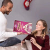 Mujer sonríe mientras hombre sostiene calendario de adviento rosa para niños y jóvenes.