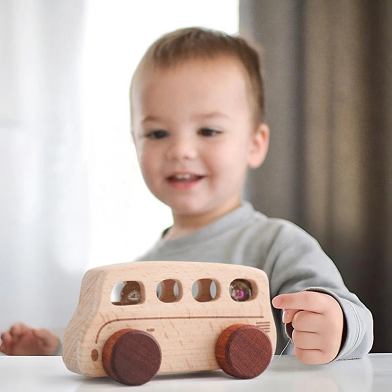 A toddler is holding a light wooden cart toy designed for pushing and play.