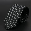 Corbata estampada con patrón de cheurones en blanco y negro, enrollada sobre una superficie oscura.