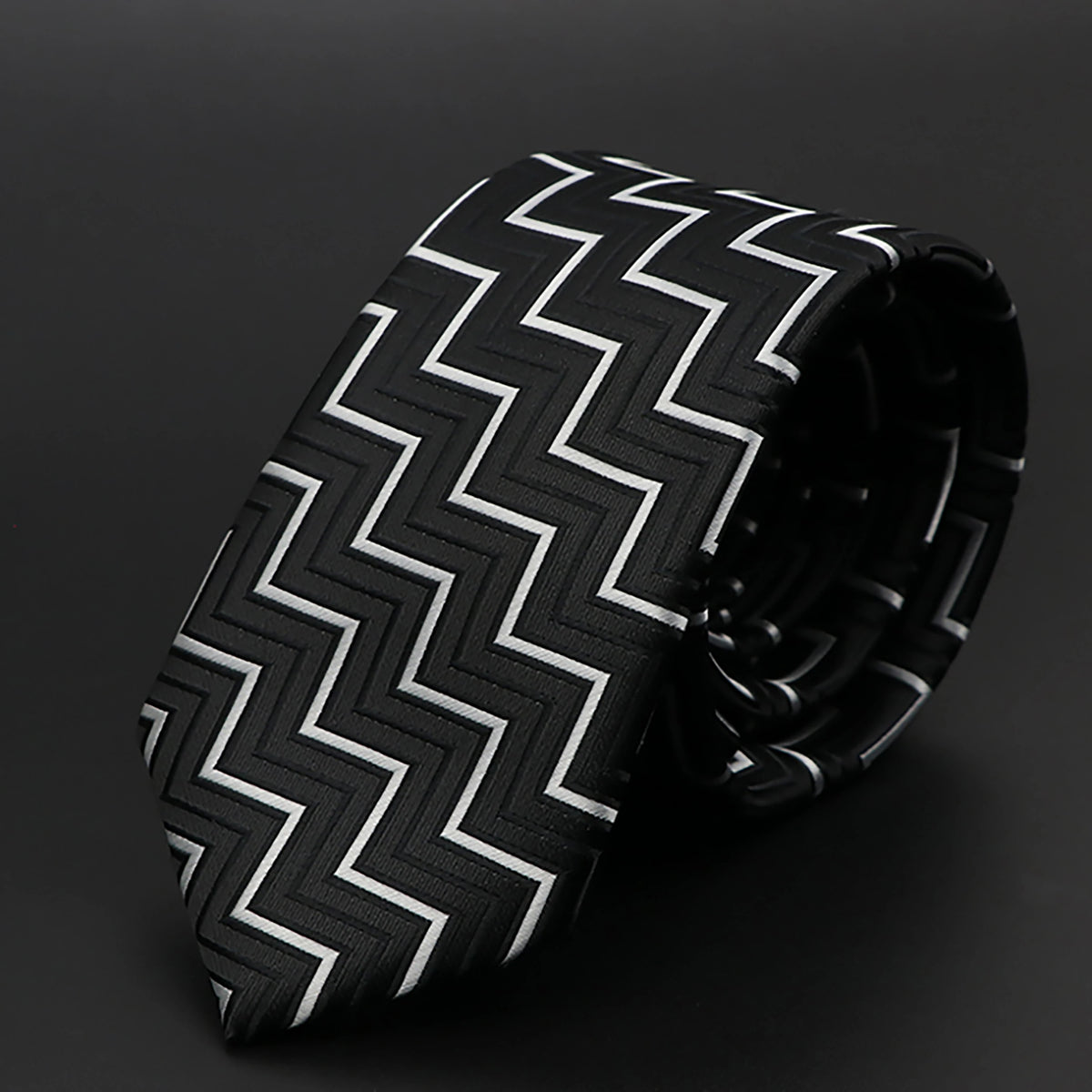 Corbata estampada con patrón de cheurones en blanco y negro, enrollada sobre una superficie oscura.