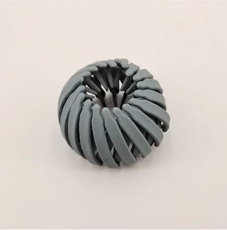 مشبك شعر على شكل عش طائر هندسي باللون الرمادي الداكن مع تصميم ملتف ومزخرف.