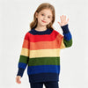 A young girl wearing a colorful rainbow striped knit sweater and dark pants, waving her hand.