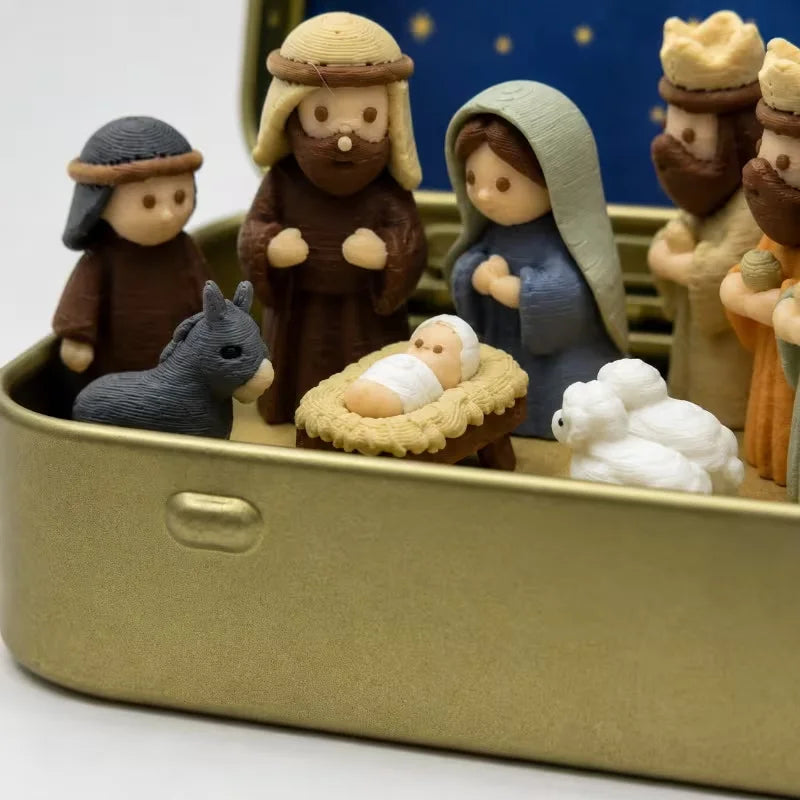 Miniature nativity scene featuring figures, including shepherds, a baby, and an animal, displayed in a gold metal box.