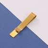 A gold metal tie clip lying diagonally on a blue and white background.
