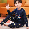 A young boy wearing a navy blue cotton pajama set featuring a smiling astronaut design.