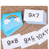 A set of white multiplication flashcards showing various multiplication problems like 9x7 and 9x8 on a burlap surface.