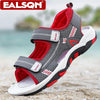 A pair of gray and red boys' breathable summer sport sandals with adjustable straps resting on a sandy beach.