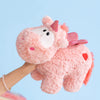 A hand is holding a pink unicorn plush pillow with pink accents against a light blue background.