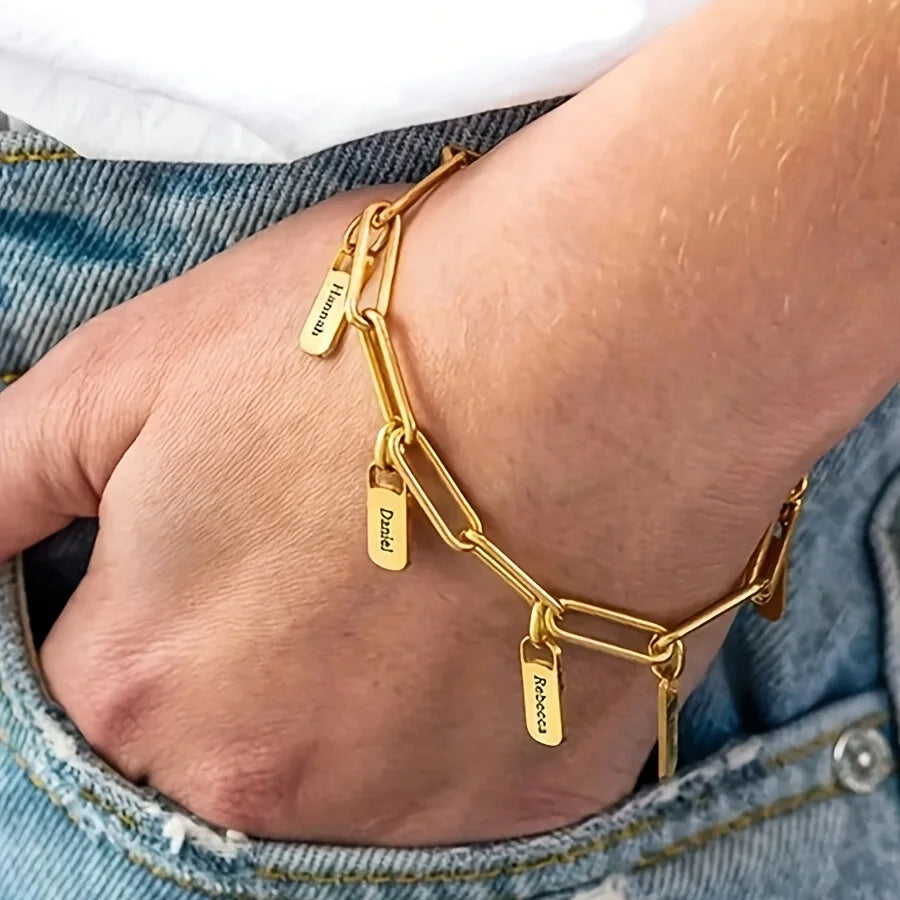 Pulsera de acero inoxidable bañada en oro con nombre y cadena ajustable, vista en una muñeca.
