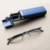 A pair of blue-framed reading glasses with a visible blue light filter resting on a neutral surface.
