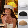 A woman wearing a white straw pillbox sun hat while holding a glass of wine.