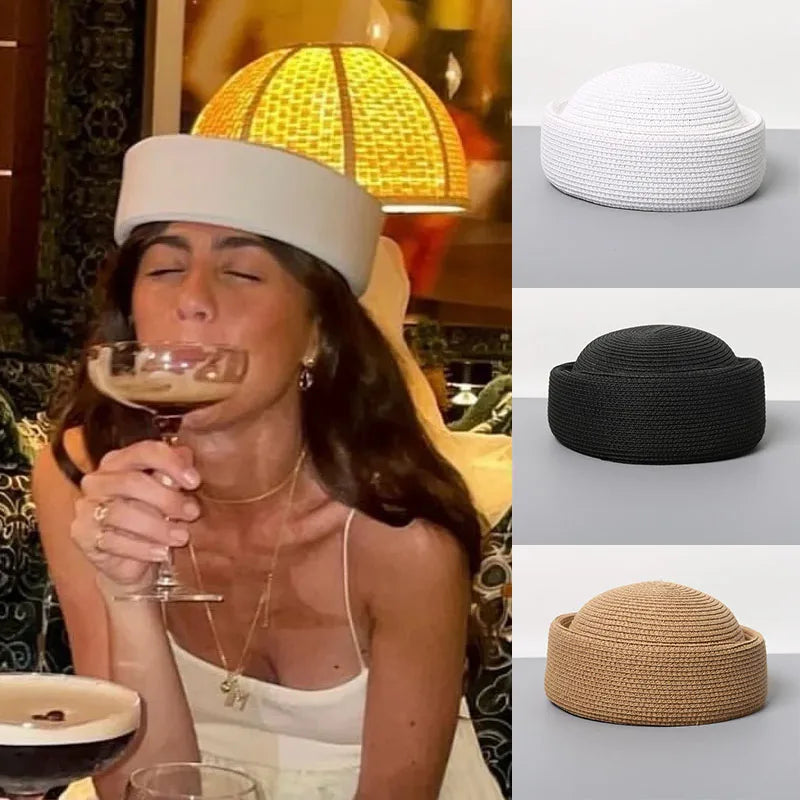 A woman wearing a white straw pillbox sun hat while holding a glass of wine.