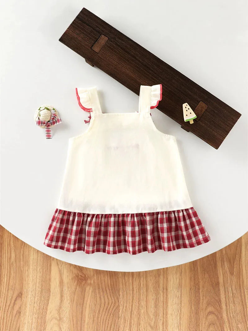 A white kids summer pinafore dress with red trim and a red and white checkered ruffle skirt, displayed on a wooden hanger.