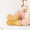 A pair of yellow cartoon non-slip baby socks for toddlers shown on a person's foot.
