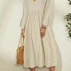 A woman wearing a beige cotton-linen blend dress with bell sleeves and a V-neck, standing indoors.