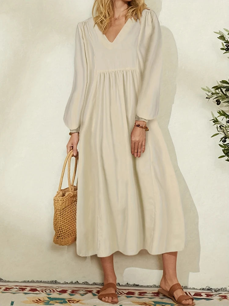 A woman wearing a beige cotton-linen blend dress with bell sleeves and a V-neck, standing indoors.