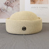 A beige straw pillbox sun hat with a wide brim resting on a gray surface.