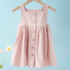 A pink sleeveless cotton dress for a toddler girl hanging on a wooden hanger against a light blue background.
