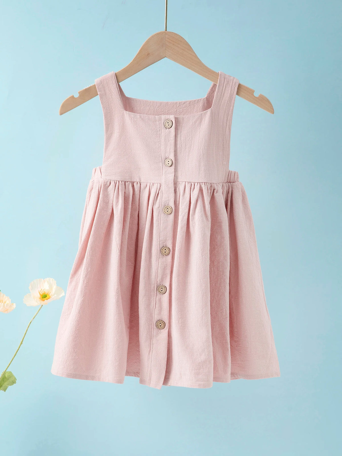 A pink sleeveless cotton dress for a toddler girl hanging on a wooden hanger against a light blue background.