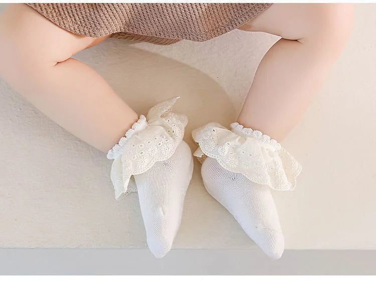 A pair of white lace princess baby socks with non-slip grips shown on a person's foot.