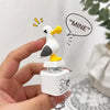 Eine Hand hält einen weißen Vogel-Anhänger mit gelbem Schnabel und LED-Licht an der Spitze, vor weißem Hintergrund.