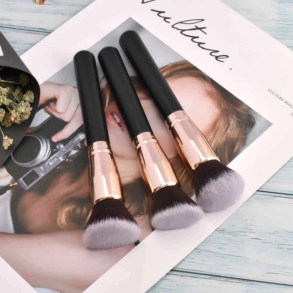 Three professional makeup brushes with gold ferrules and grey bristles displayed on a white background.