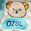 A white fleece pajama top featuring a cute bear face and a light blue chest patch with the text OZSL.