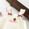 A cream-colored kids summer pinafore dress with strawberry and bunny print, featuring red embroidery and ruffled trim.