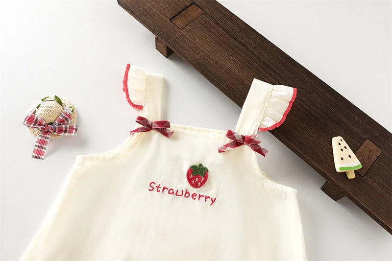 A cream-colored kids summer pinafore dress with strawberry and bunny print, featuring red embroidery and ruffled trim.