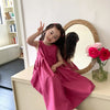 A young girl wearing a pink cotton sleeveless sundress is posing with a peace sign in front of a mirror.