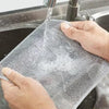A hand is using a scratch-free microfiber cleaning cloth to wash dishes in a kitchen sink.