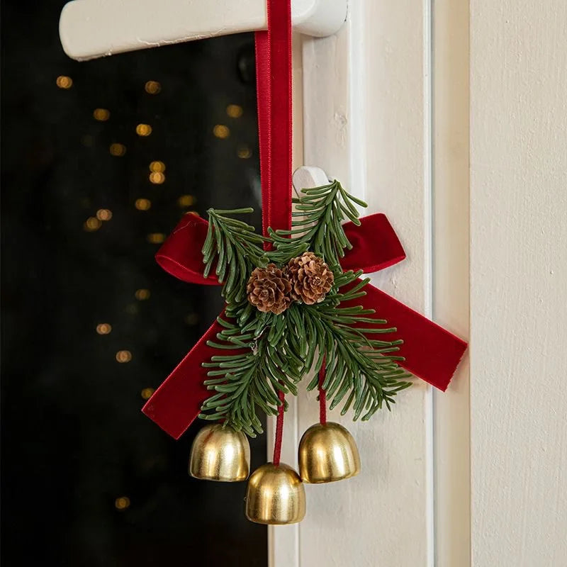 Un porte-nœud en velours rouge avec une branche de pin verte et des grelots dorés suspendus à un cadre de porte blanc.