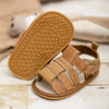 A pair of tan baby summer sandals with non-slip rubber soles resting on a light wooden surface.