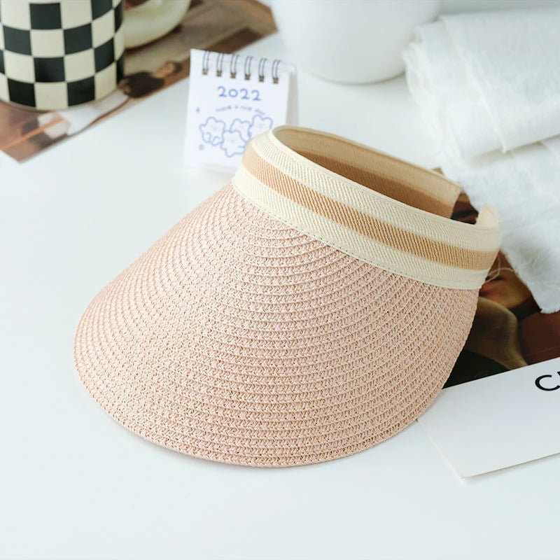 A woven straw sun hat with a beige brim and band is displayed on a white surface.