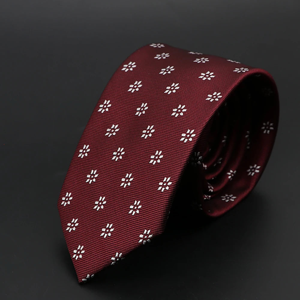 Corbata estampada rojo oscuro con motivos florales blancos, enrollada sobre fondo oscuro.