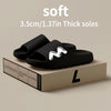 Black soft EVA slide slippers with thick soles shown on a wooden box.