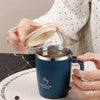 A hand holds a dark blue stainless steel insulated travel mug with a handle on a white surface.