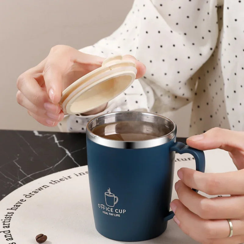 A hand holds a dark blue stainless steel insulated travel mug with a handle on a white surface.