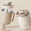 A beige double wall insulated stainless steel travel mug with a removable lid and handle shown in a studio setting.