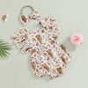 A white baby romper with a cow print pattern and matching headband, laid on a light surface.