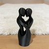 Sculpture noire de deux figures entrelacées reposant sur un tapis moelleux beige clair.