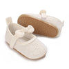 A pair of soft non-slip baby first walker shoes in off-white fabric with a tan sole and a decorative bow detail.