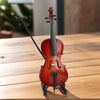 Un violoncelle miniature en bois avec un archet posé sur une surface en bois clair.