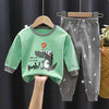 A green cartoon dinosaur long-sleeved shirt and matching gray dinosaur pajama pants displayed on a hanger.