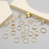 A collection of gold rings featuring various designs including hearts, geometric shapes, crosses, and pearl accents.