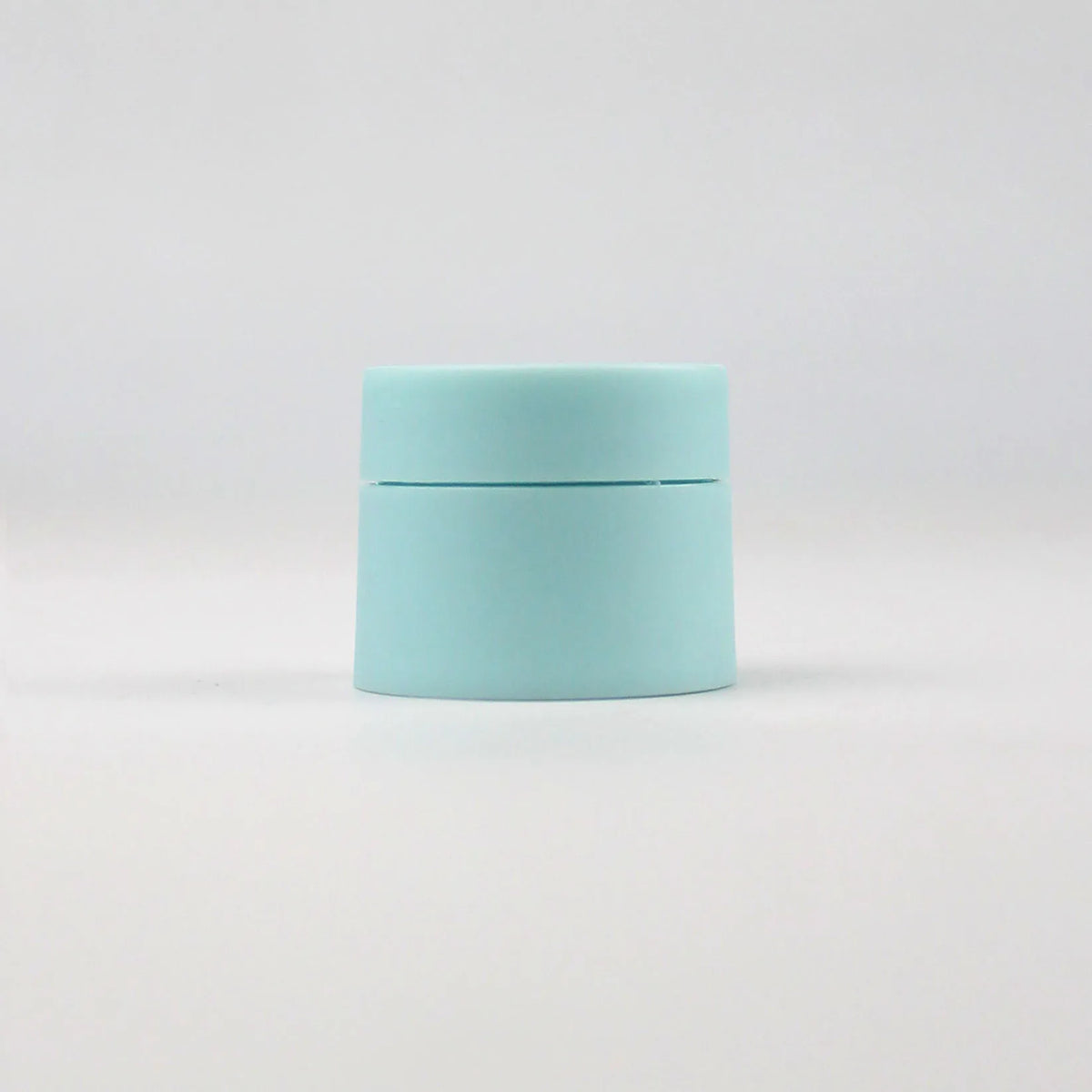 A light blue refillable travel face cream jar with a white lid, shown against a white background.