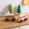 A hand-pushed wooden cart toy for toddlers with a green handle and a small green tree decoration.