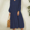 A woman wearing a navy blue cotton-linen blend dress with a V-neck and bell sleeves, standing indoors.