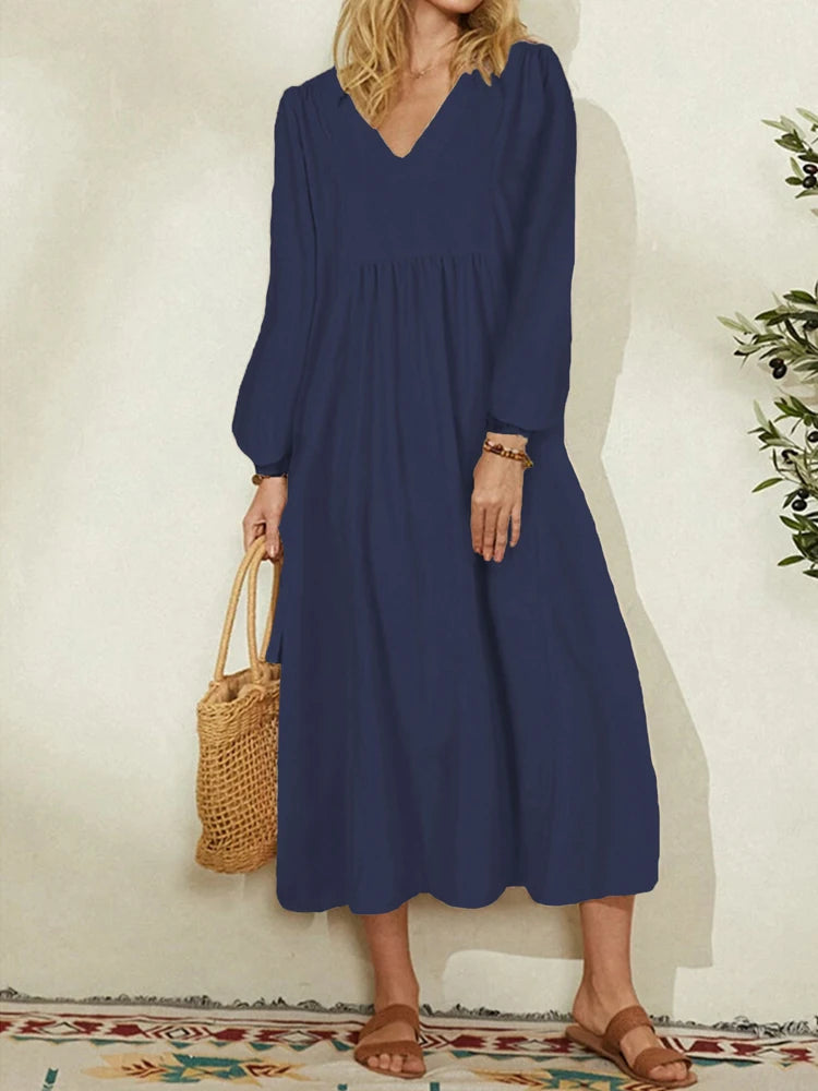 A woman wearing a navy blue cotton-linen blend dress with a V-neck and bell sleeves, standing indoors.
