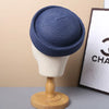 A navy blue straw pillbox sun hat displayed on a wooden mannequin.